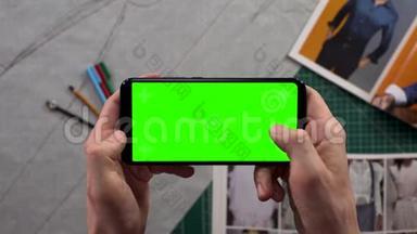 男人的特写镜头`双手拿着智能手机，背景衣柜里有一个水平的绿色屏幕，准备着衣服